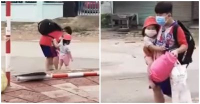 Cha mẹ là F0, bé trai một tay xách đồ, một tay bế em đi cách ly